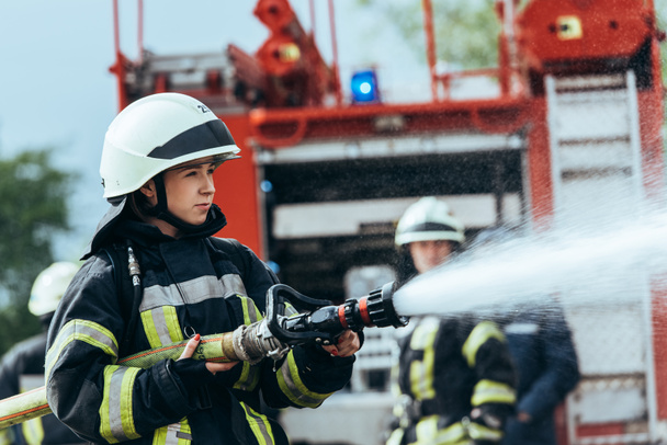 female firefighter with water hose extinguishing fire on street - Photo, Image