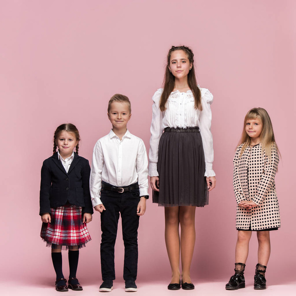Cute stylish children on pink studio background. The beautiful teen girls and boy standing together - Фото, изображение