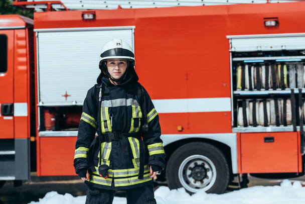 female firefighter in protective uniform standing on street with red fire truck behind - Fotoğraf, Görsel