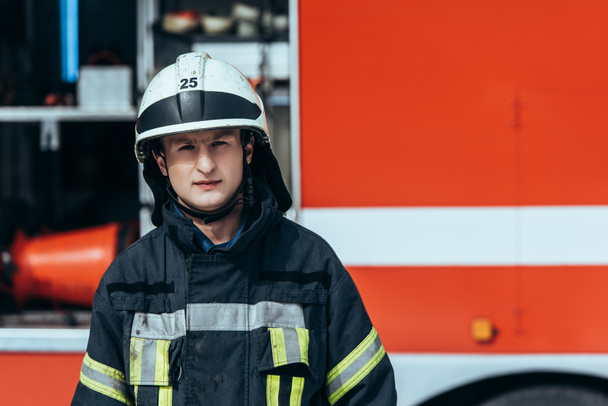 portrait de pompier en uniforme debout dans la rue avec camion de pompiers rouge derrière
 - Photo, image