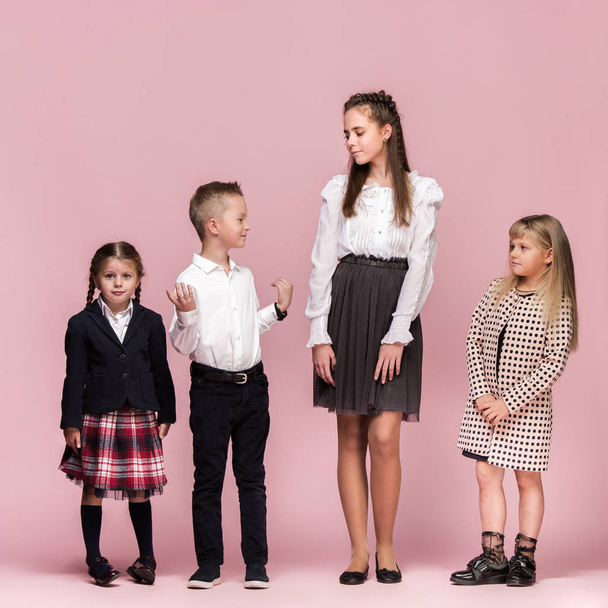 Cute stylish children on pink studio background. The beautiful teen girls and boy standing together - 写真・画像