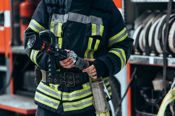 cropped shot of firefighter in protective uniform holding water hose in hands - Photo, Image