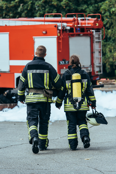 back view of firefighters in fireproof uniform walking on street with fire truck behind - Fotografie, Obrázek