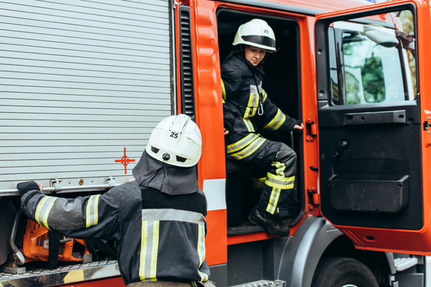 Teilansicht von Feuerwehrleuten in Helmen an Feuerwehrauto auf der Straße - Foto, Bild