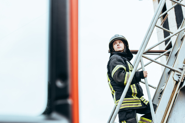 female firefighter in protective uniform and helmet standing on ladder on street - Photo, Image