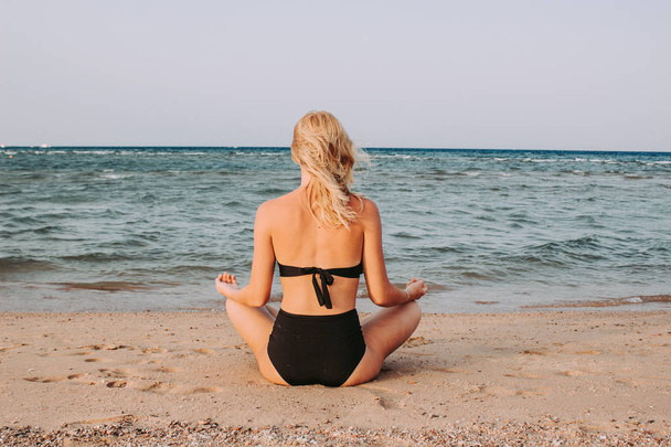 Young summer woman meditates on the sea sitting on the beach - Foto, afbeelding