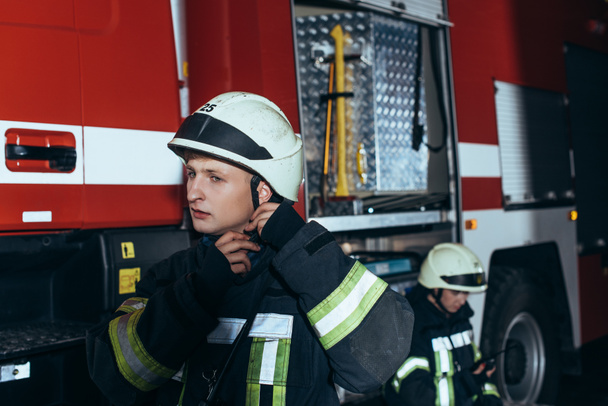 casco de control de bomberos con colega detrás en el departamento de bomberos
 - Foto, Imagen