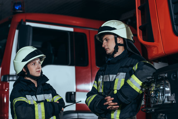 Feuerwehrleute in feuerfester Uniform und Helmen schauen sich am Feuerwehrhaus an - Foto, Bild
