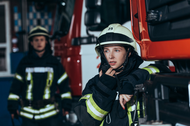 fuoco selettivo di pompiere donna che parla su apparecchio radio portatile con collega dietro a pompieri
 - Foto, immagini