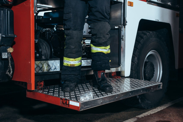 partial view of firefighter in fireproof uniform standing on truck at fire station - Fotó, kép