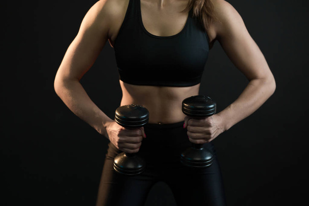 beautiful young girl goes in for sports with dumbbells on a black background - Foto, Imagen