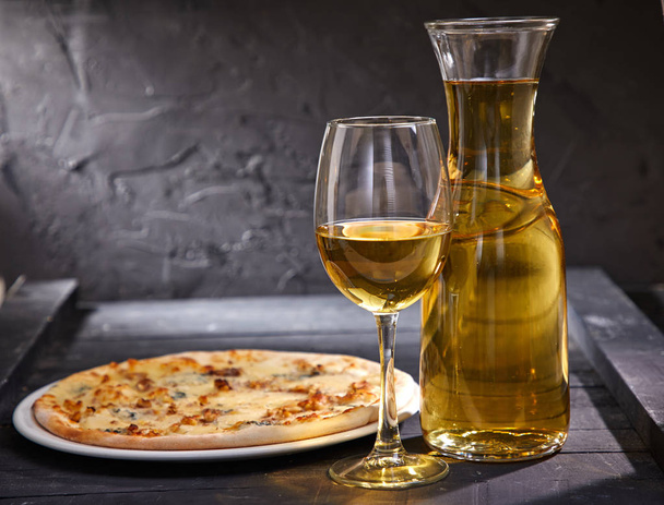 wineglass and decanter with cold white wine and pizza on wooden background, close-up   - Photo, image