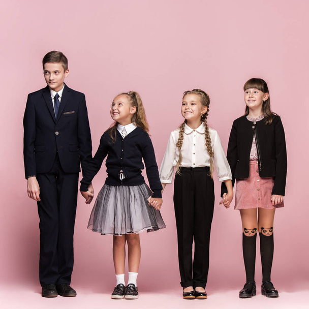 Cute stylish children on pink studio background. The beautiful teen girls and boy standing together - Zdjęcie, obraz