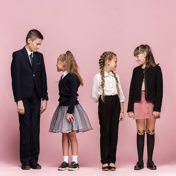 Cute stylish children on pink studio background. The beautiful teen girls and boy standing together - Фото, изображение