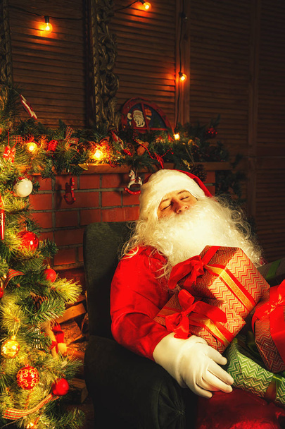 Tired Santa Claus sleeps near the Christmas tree at home. - Zdjęcie, obraz