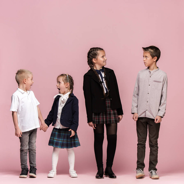 Cute stylish children on pink studio background. The beautiful teen girls and boy standing together - Foto, Imagen