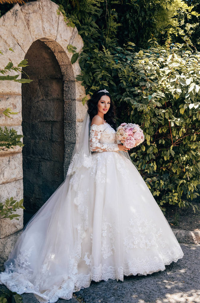 fashion outdoor photo of beautiful bride with dark hair in luxurious wedding dress posing in elegant villa - Photo, Image