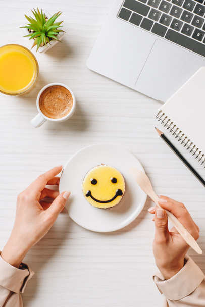 обрізане зображення бізнес-леді, що їсть торт із символом посмішки за столом з апельсиновим соком та чашкою кави в офісі
  - Фото, зображення