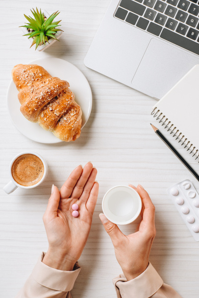 részleges kilátás nyílik üzletasszony figyelembe pirula, croissant és kávé csésze hivatalban asztalnál ebéd előtt  - Fotó, kép