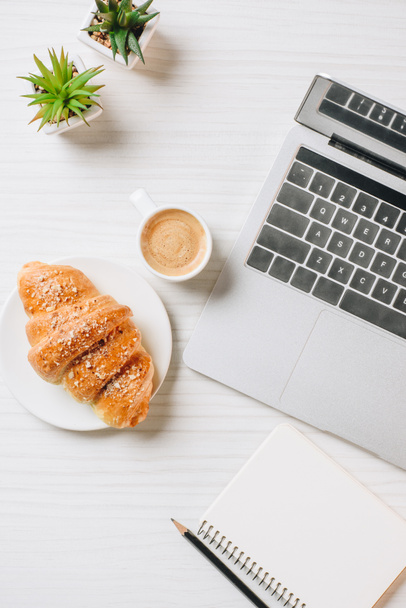 top view of workplace with laptop, empty textbook, croissant and coffee cup in office  - Fotoğraf, Görsel