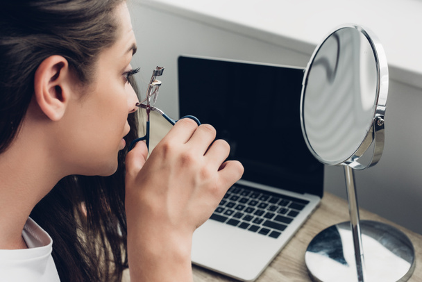 close-up portrait of young transgender woman doing makeup with lash curler at home - Zdjęcie, obraz