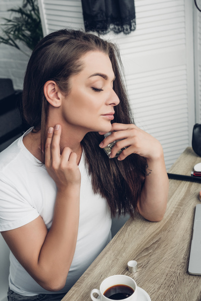 close-up portrait of young transgender woman applying perfume on neck at home - Photo, Image