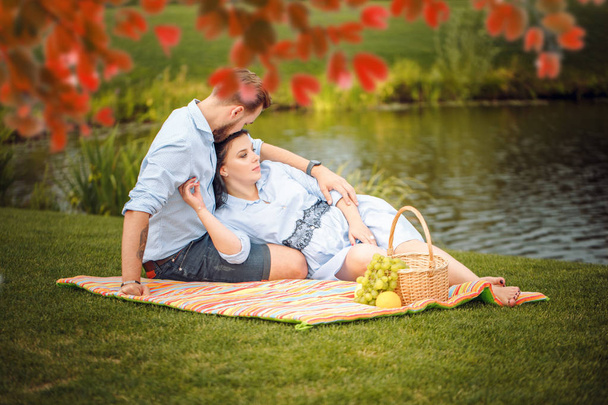 Щасливий радісний молодий сімейний чоловік і його вагітна дружина розважаються разом на відкритому повітрі, на пікніку в літньому парку, в сільській місцевості. чекає дитину
 - Фото, зображення