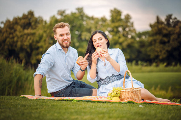 Happy joyful young family husband and his pregnant wife having fun together outdoors, at picnic in summer park, countryside. waiting for a child - Foto, imagen