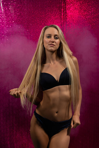 Beautiful slender tanned blonde in black lingerie on pink glitter walls - Photo, Image