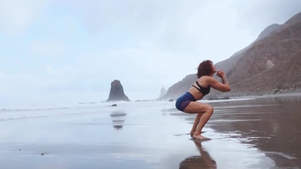 Fit žena trénovat nohy s jeho cvičení skákání squats cvičení. Fitness trénink dělá kardio cvičení na letní oceán bílý písek pláž dělá výbušné skoky a burpees aktivovat glutes. - Záběry, video