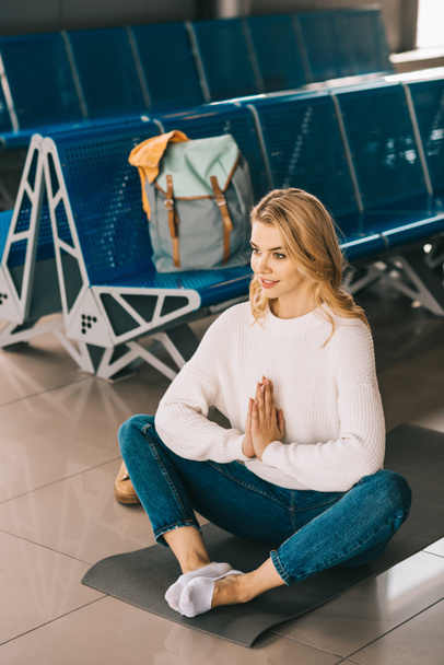 wysoki kąt widzenia uśmiechnięta młoda kobieta medytacji w pozycji lotosu, podczas lotu czeka w terminalu lotniska - Zdjęcie, obraz