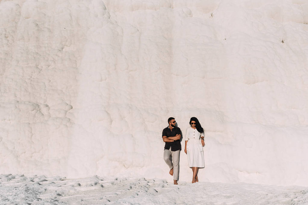 Guy and girl standing against the wall and posing in front of the camera. Wedding trip the newlyweds. A couple in love travels to Turkey, Pamukkale. Man and woman at sunset. Stylish couple in love - Foto, imagen