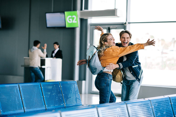 cheerful young couple with backpacks hugging in airport terminal   - Foto, afbeelding