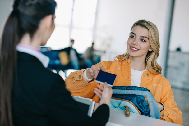 rajattu kuva työntekijän ja hymyilevä nuori nainen asiakirjoja lähtöselvitystiskillä lentokentällä
 - Valokuva, kuva