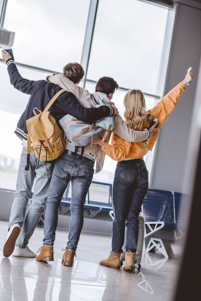 vue arrière de jeunes amis heureux avec passeports étreignant et levant la main à l'aéroport
 - Photo, image