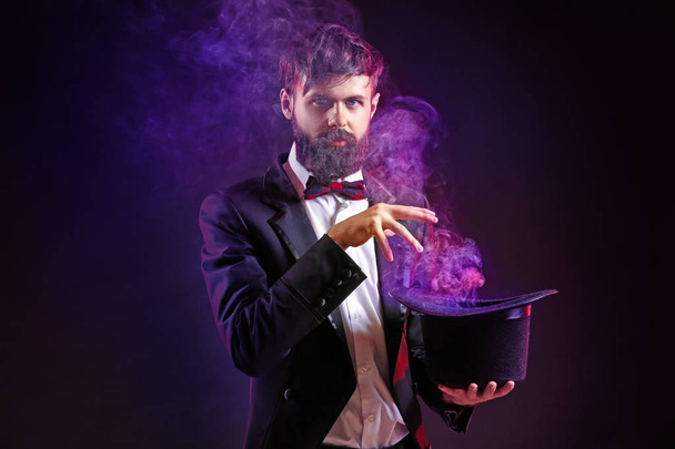 Zauberer zeigt Tricks mit Hut auf dunklem Hintergrund - Foto, Bild