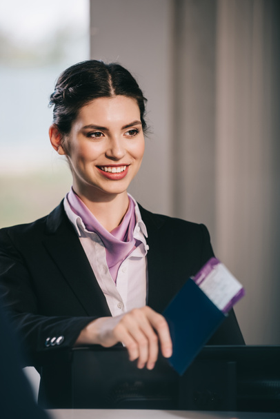 hermoso sonriente joven trabajador del aeropuerto con pasaporte con tarjeta de embarque en el mostrador de facturación
 - Foto, Imagen
