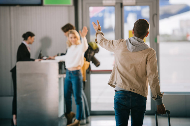 young friends waving hands at check-in desk in airport  - Фото, зображення