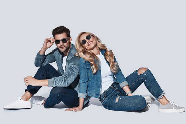 fashionable man and woman in denim wear posing in studio and sitting on floor  - Foto, Imagen
