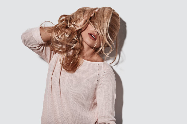 blonde woman covering face with hair while standing against grey background - Φωτογραφία, εικόνα