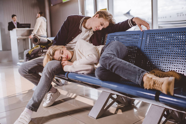 空港でフライトを待っている間一緒に寝ている若いカップル - 写真・画像