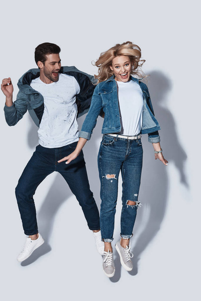 Crazy in love, Full length of beautiful young couple smiling while jumping against grey background - Fotoğraf, Görsel