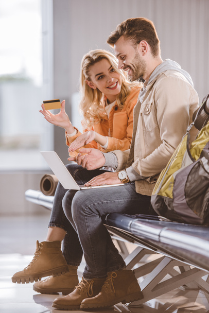 hymyilevä nuori nainen osoittaa luottokortin onnellinen mies käyttää kannettavaa lentoasemalla
 - Valokuva, kuva