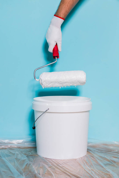 Image of paint can and man holding paint roller in front of blue wall. - Fotoğraf, Görsel