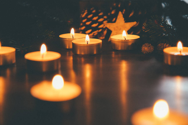 Burning Christmas candles on the table with pine cones, fir branches, decoration star and lights bokeh. Film grain effect added - Foto, Imagem