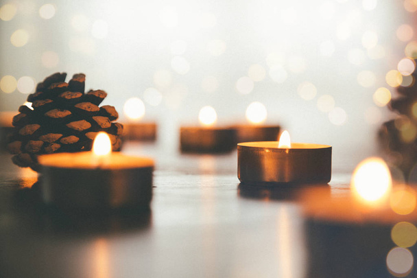 Burning Christmas candles on the table with pine cones and lights bokeh. Film grain effect added - Foto, Imagem