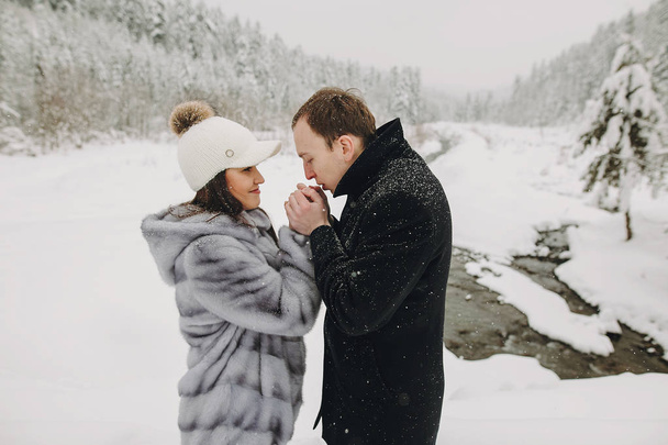 雪山を受け入れる愛のスタイリッシュなカップル。優しく、抱き合ったりキスしたり幸せな家族の冬の山や森の手します。休暇は一緒に - 写真・画像