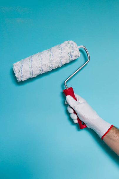 Image of man holding paint roller in front of blue wall. - 写真・画像