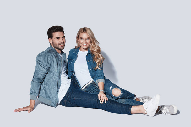 smiling stylish couple looking at camera and smiling while sitting against grey background - Foto, imagen
