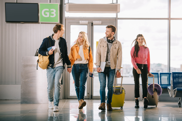 glimlachend jonge vrienden met rugzakken en koffers in de luchthaventerminal - Foto, afbeelding